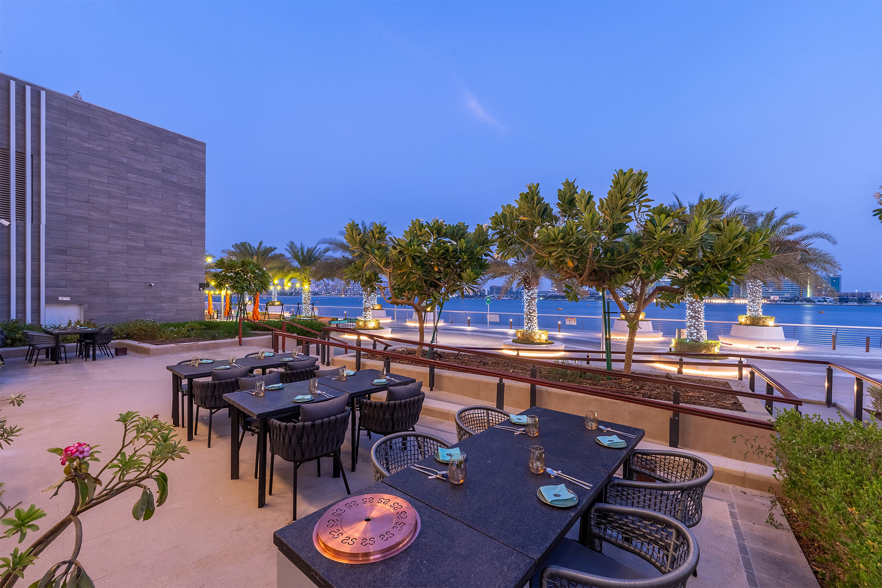 Outside seating, set of tables, blue twilight sky, palm trees and building on side
