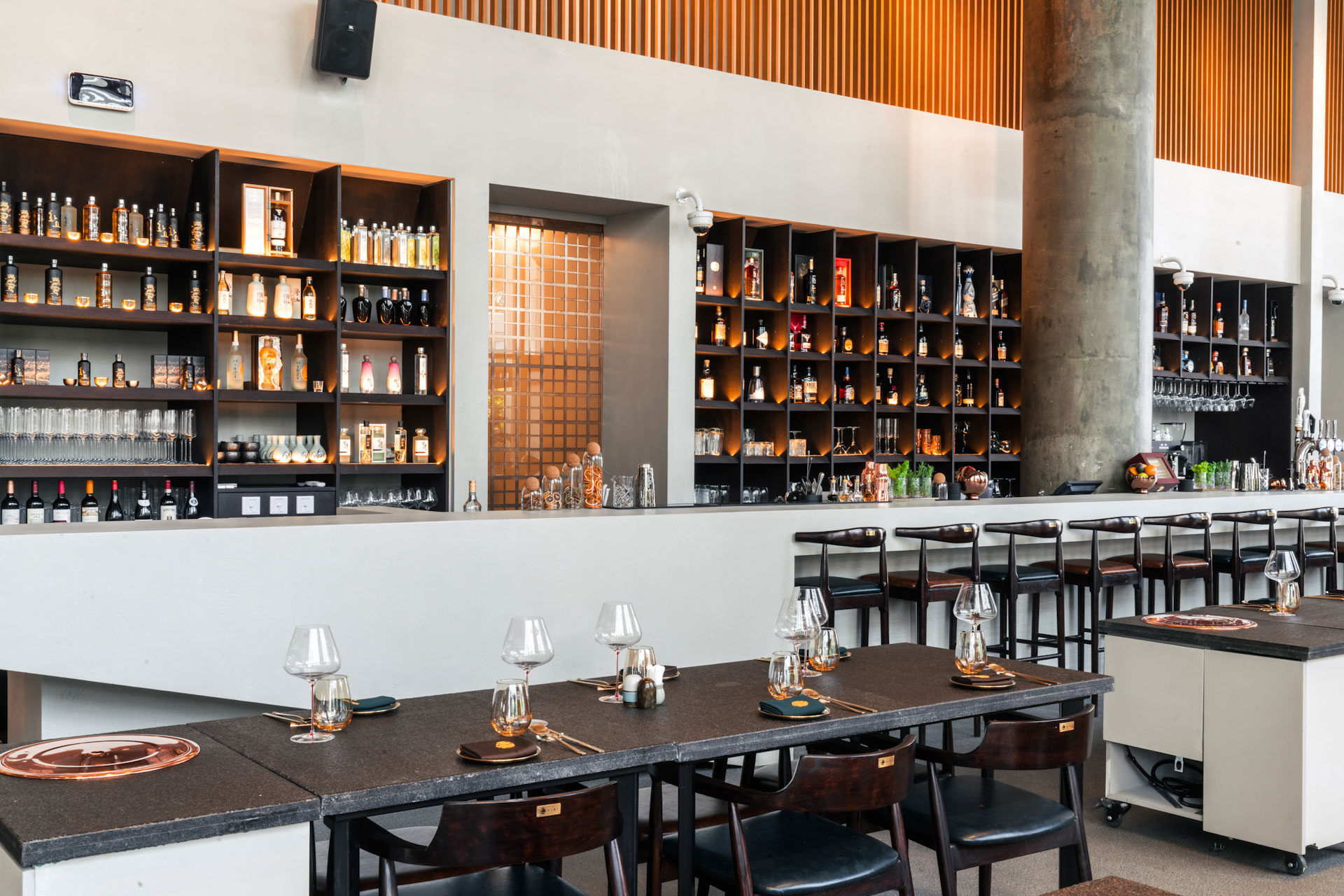Dining table on foreground and bar at the background displaying set of wines and beverages